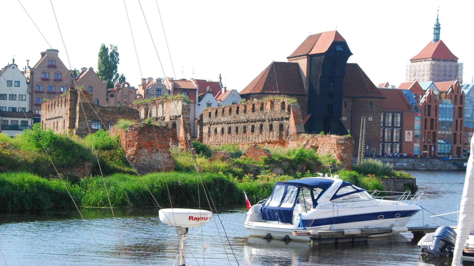 View on the Crane (Żuraw) from the other side of the riverbank. The Crane of Gdańsk is one of the important landmarks. In summertime there are many little yachts harbouring in the cute yacht harbour in Old Town. You can also see the smaller merchants' houses and the ruins, a reminiscence of what was destroyed during World War II. View on the Crane (Żuraw) from the other side of the riverbank. The Crane of Gdańsk is one of the important landmarks. In summertime there are many little yachts harbouring in the cute yacht harbour in Old Town. You can also see the smaller merchants' houses and the ruins, a reminiscence of what was destroyed during World War II.